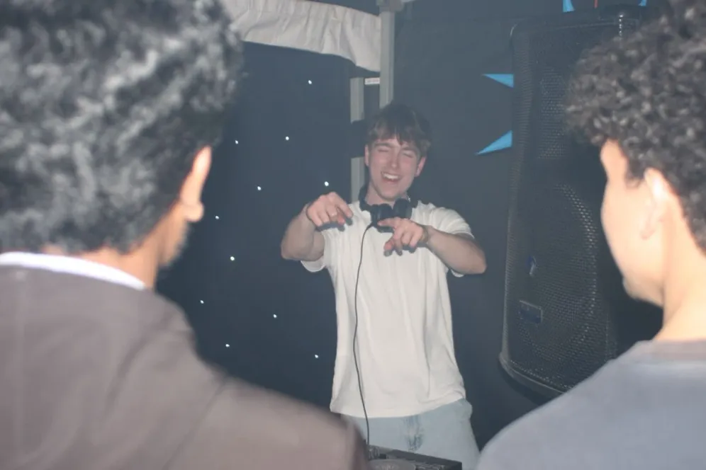 MC Cal behind the DJ booth, pointing at the crowd